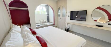 Una habitación de hotel moderna con una cama grande, televisión, espejo y una pequeña mesa junto a la ventana.
