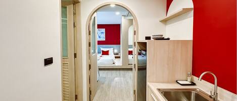 A hotel room with a kitchenette, a bed with red pillows, and a red accent wall.