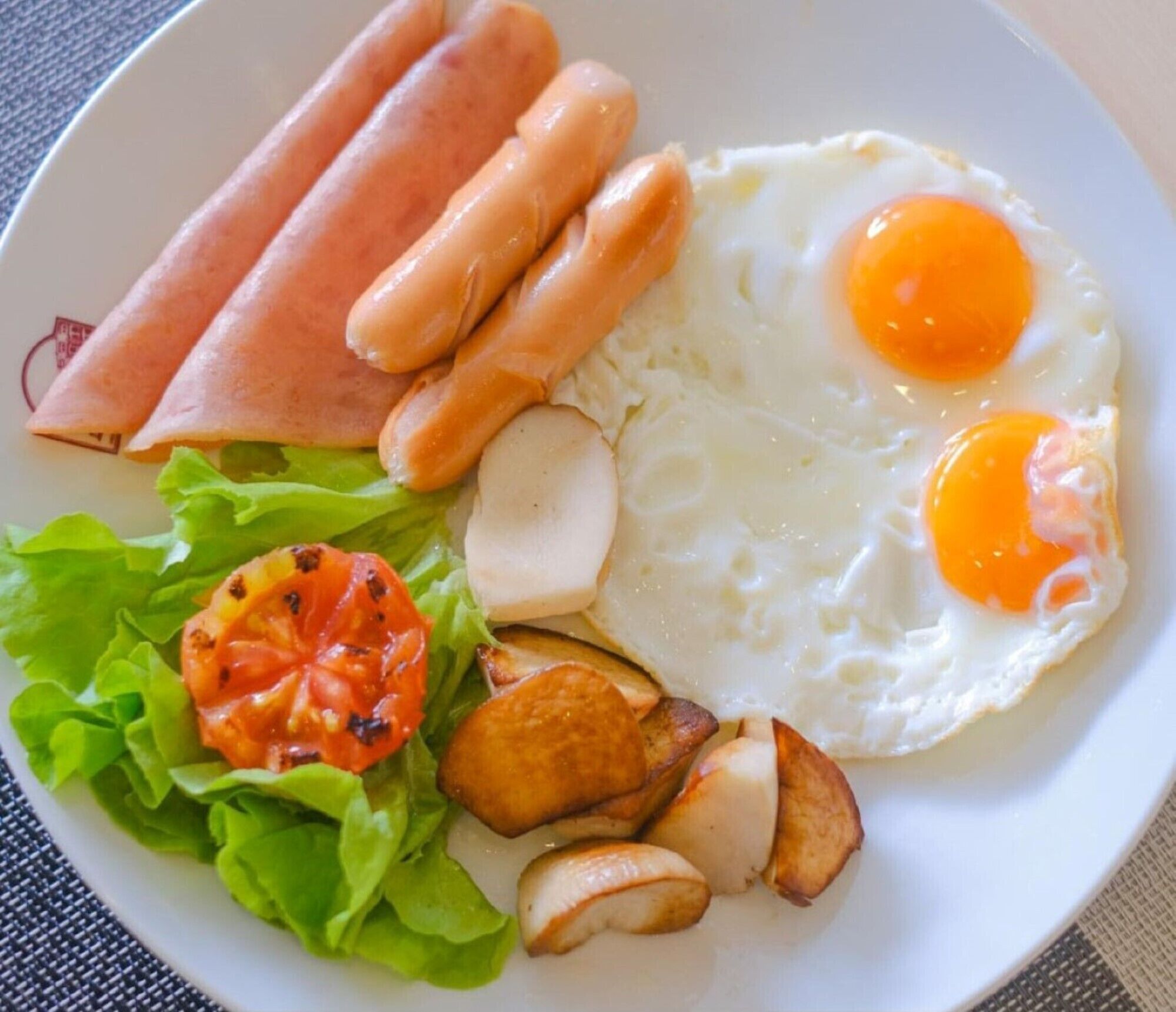 A plate with eggs, ham, sausages, lettuce, and roasted potatoes.