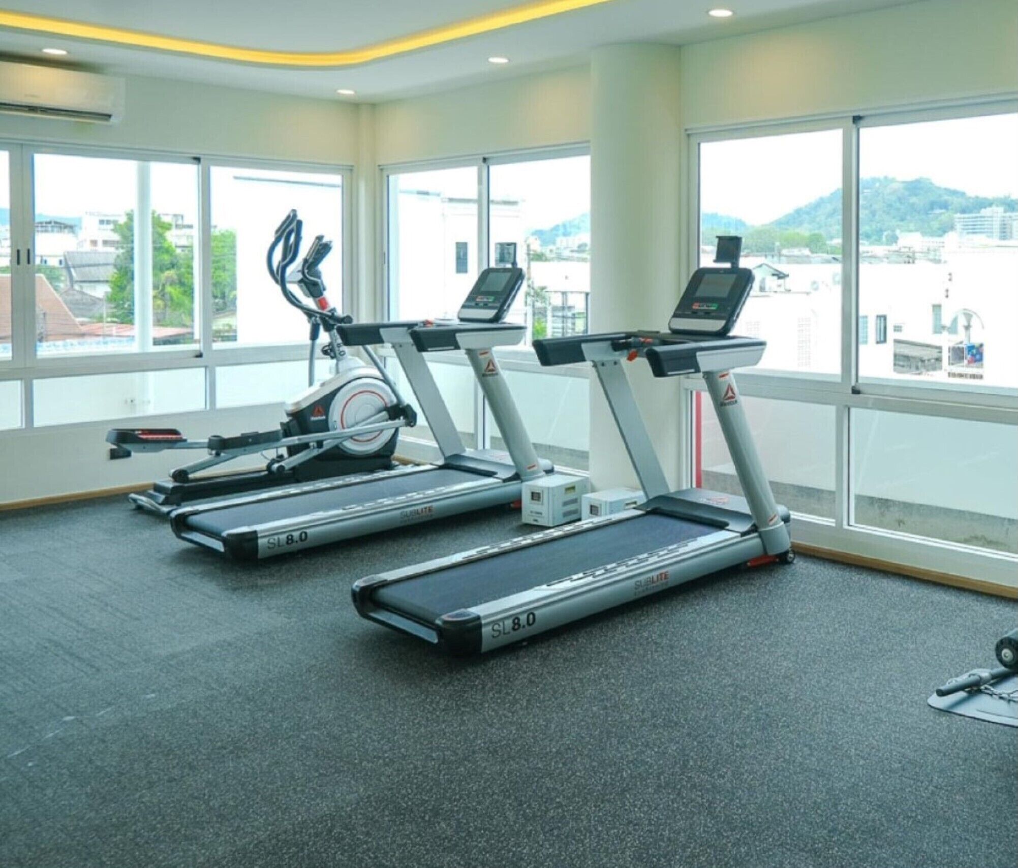 A gym with two treadmills and a stationary bike, large windows, and a view of buildings and hills.
