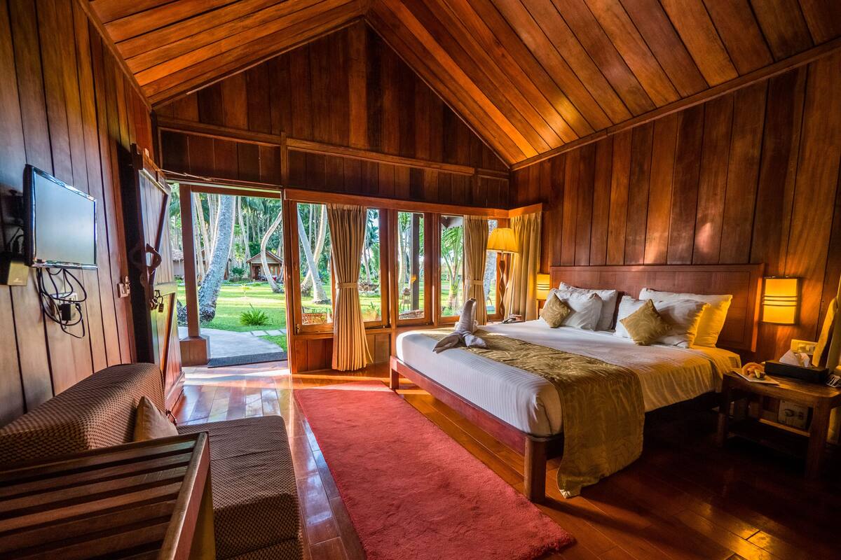A spacious wooden room with a large bed, a wooden bench, and a red rug.