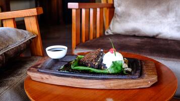 A wooden table with a plate of food, a cup of tea, and a cushion on a chair.
