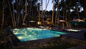 Una piscina rodeada de palmeras y sillas de descanso, con vista a un edificio de resort al fondo.
