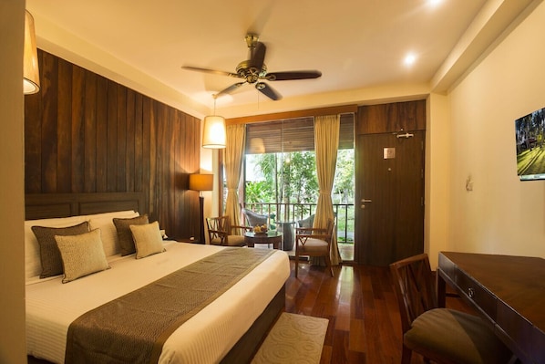 A bedroom with a large bed, a ceiling fan, a balcony with chairs, and a view of greenery outside. - Seashell Havelock (Port Blair)