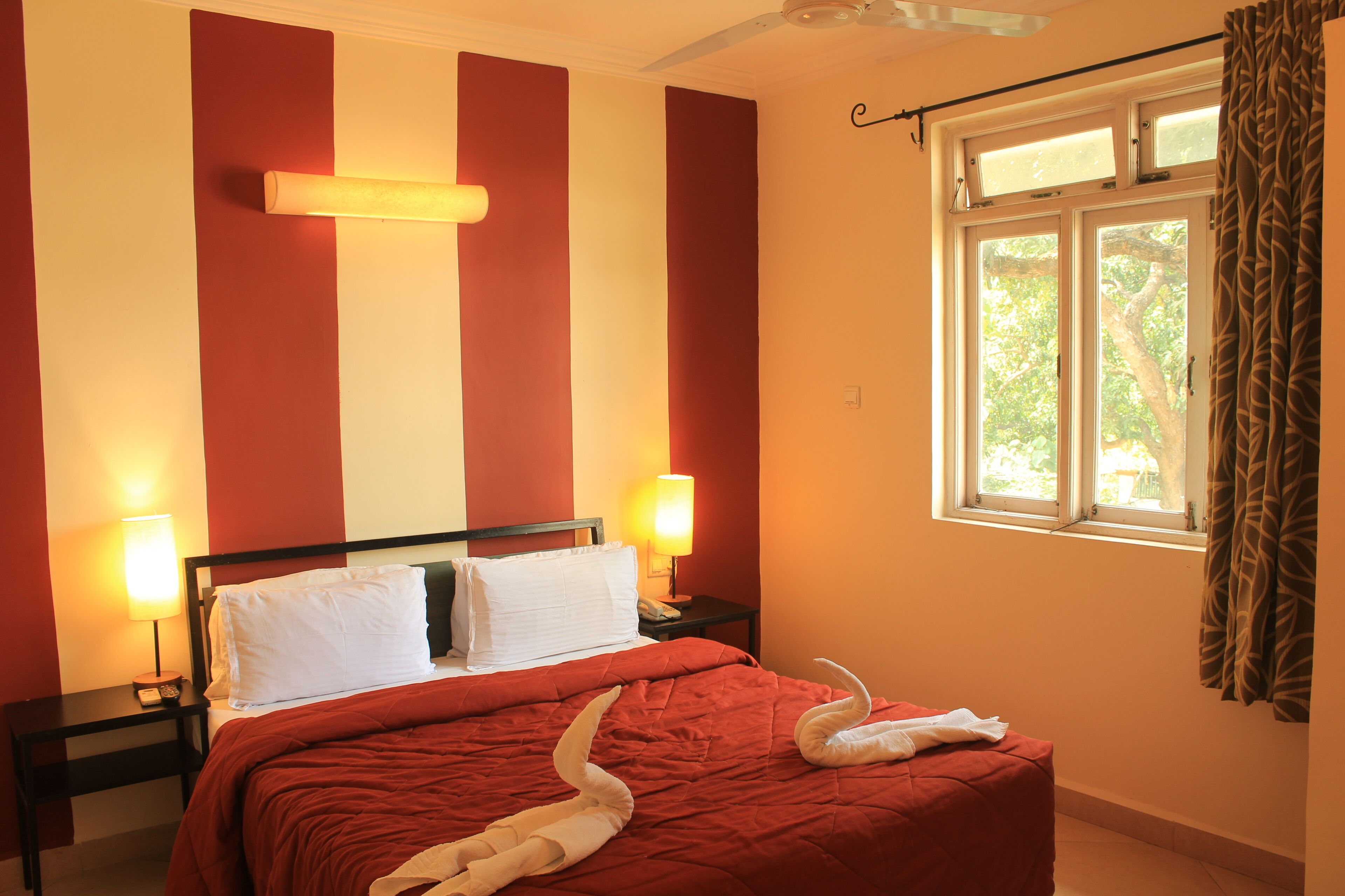 Habitación de hotel con cama, dos lámparas de noche, ventana con cortinas y pared con rayas verticales.