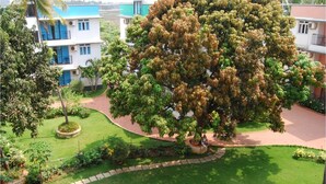 A residential area with a large tree in the center, surrounded by a well-maintained lawn and a curved pathway. - Aastha Escape Resort (Calangute)