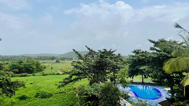 A pool surrounded by lush greenery and hills in the background. - Aastha Escape Resort (Calangute)