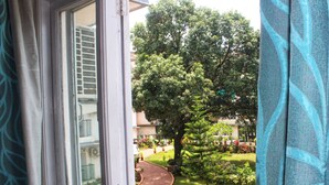 A window view of a garden with a tree and a circular planter. - Aastha Escape Resort (Calangute)