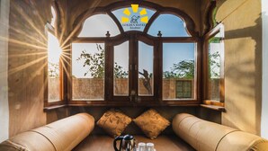 Una habitación con un ventanal grande, una bandeja con tetera, tazas y bolsitas de té, y dos almohadones.