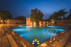 A swimming pool with a clear view of the water, surrounded by a stone deck and a brick wall. - Hotel Golden Haveli (Jaisalmer)