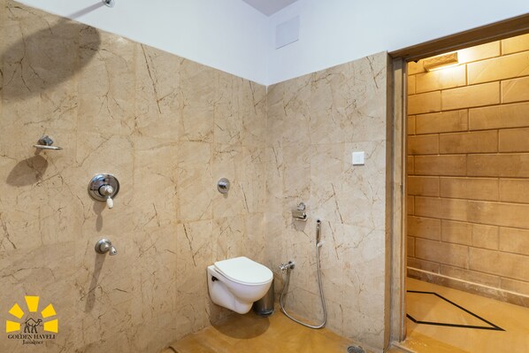 A bathroom with a marble wall, a toilet, a shower, and a wooden door. - Hotel Golden Haveli (Jaisalmer)