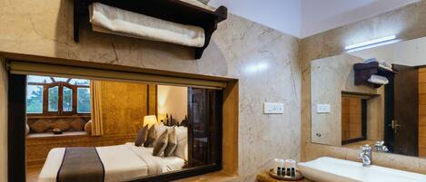 A hotel bathroom with a large mirror, a sink, and a window with a view of the room.