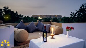 Una terraza con una mesa preparada para dos, que incluye una botella de vino Sula, una vela y un jarrón con flores.