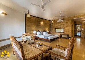 A hotel room with a bed, a dining table, chairs, a TV, and a ceiling fan. - Hotel Golden Haveli (Jaisalmer)