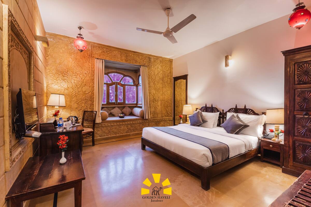 A hotel room with a large bed, a desk, a chair, a window with curtains, a ceiling fan, and a decorative lamp.