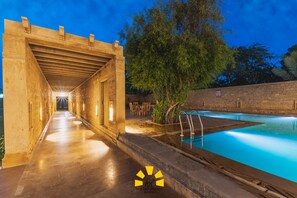 A pool area with a covered walkway and a stone wall. - Hotel Golden Haveli (Jaisalmer)