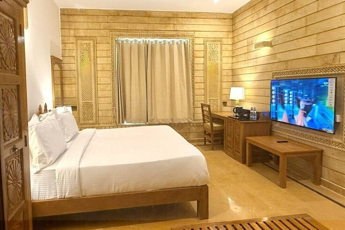 A hotel room with a large bed, a desk with a chair, a television, and a window with curtains.