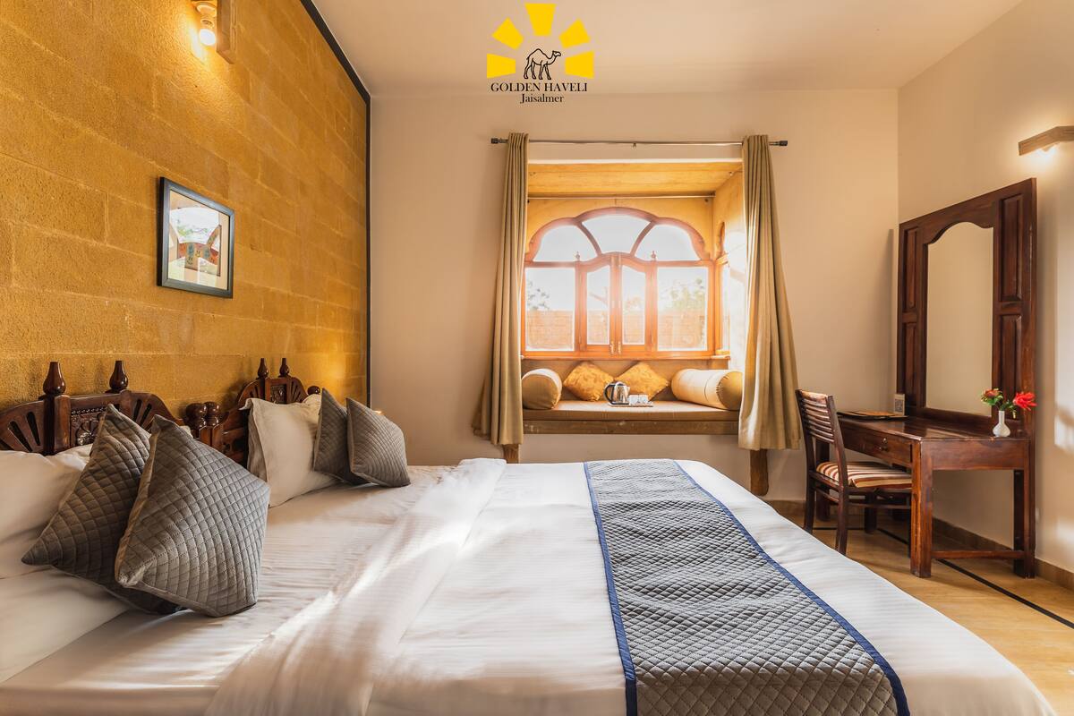 A hotel room with a large bed, a wooden desk, a chair, and a window with curtains.