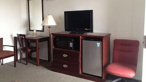 A compact hotel room with a wooden desk, a television, a microwave, a refrigerator, a red chair, and a lamp. - Budget Inn Fort Stockton (Fort Stockton)