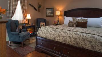 A bedroom with a large bed, a chair, a small table, a lamp, and a fireplace.