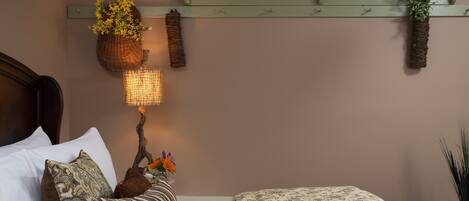 A bedroom with a bed, pillows, a bedside lamp, a shelf with decorative items, and a book on the bed.
