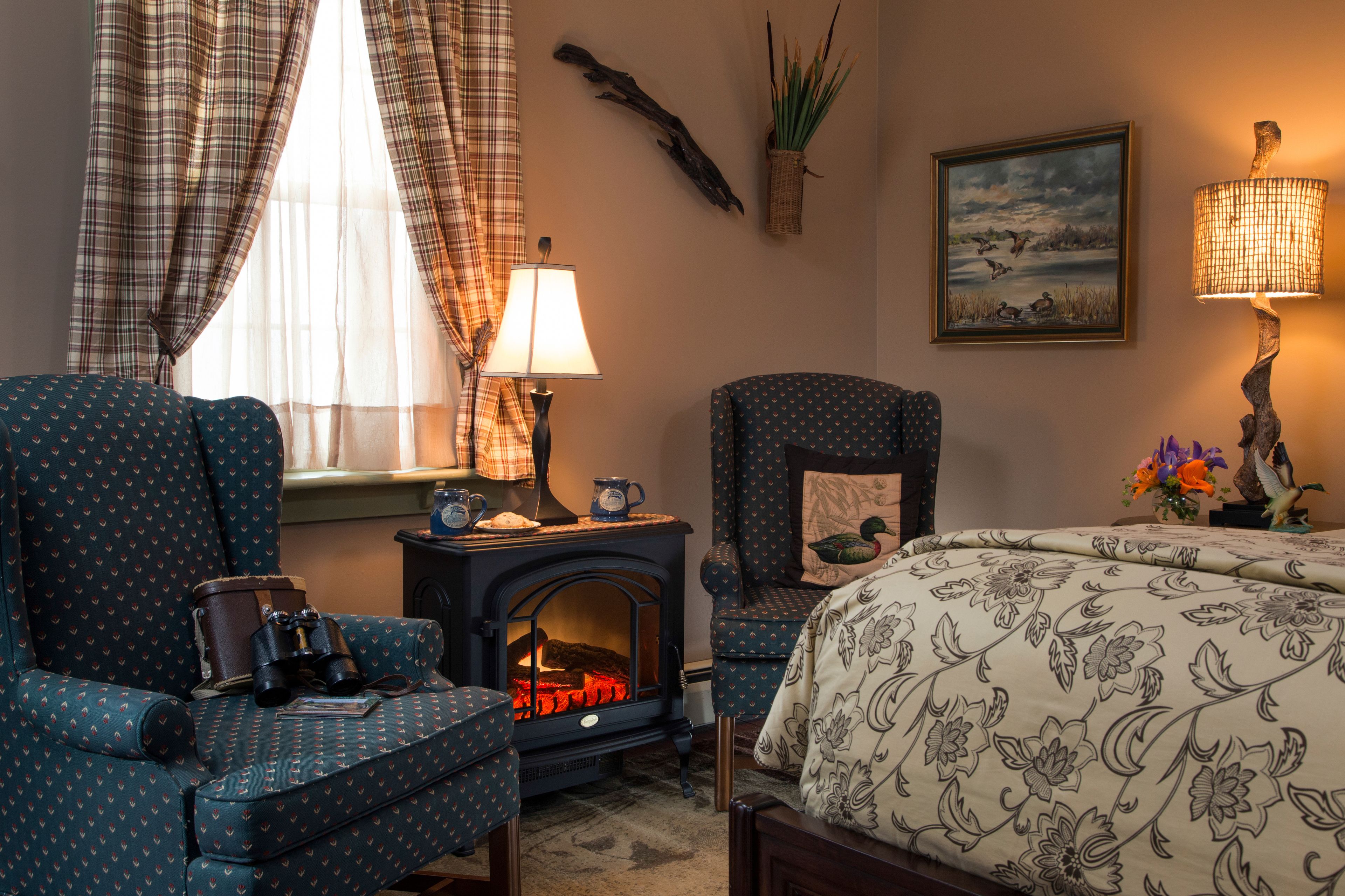 Una habitación acogedora con chimenea, cortinas escocesas, un sillón estampado y una cama con colcha de motivos florales.