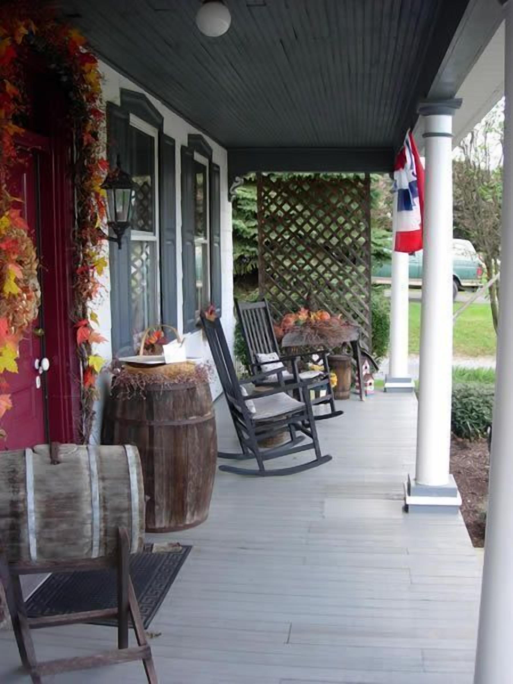 A covered porch with rocking chairs and a wooden barrel, decorated with autumn leaves.