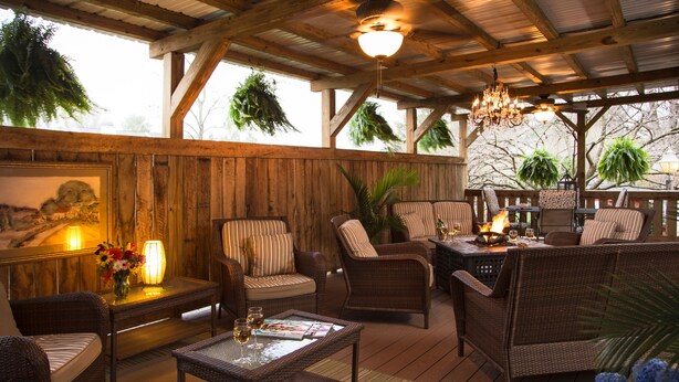 A covered outdoor seating area with wicker furniture, a table with a magazine, and a hanging plant. - 1825 Inn Bed and Breakfast (Palmyra)