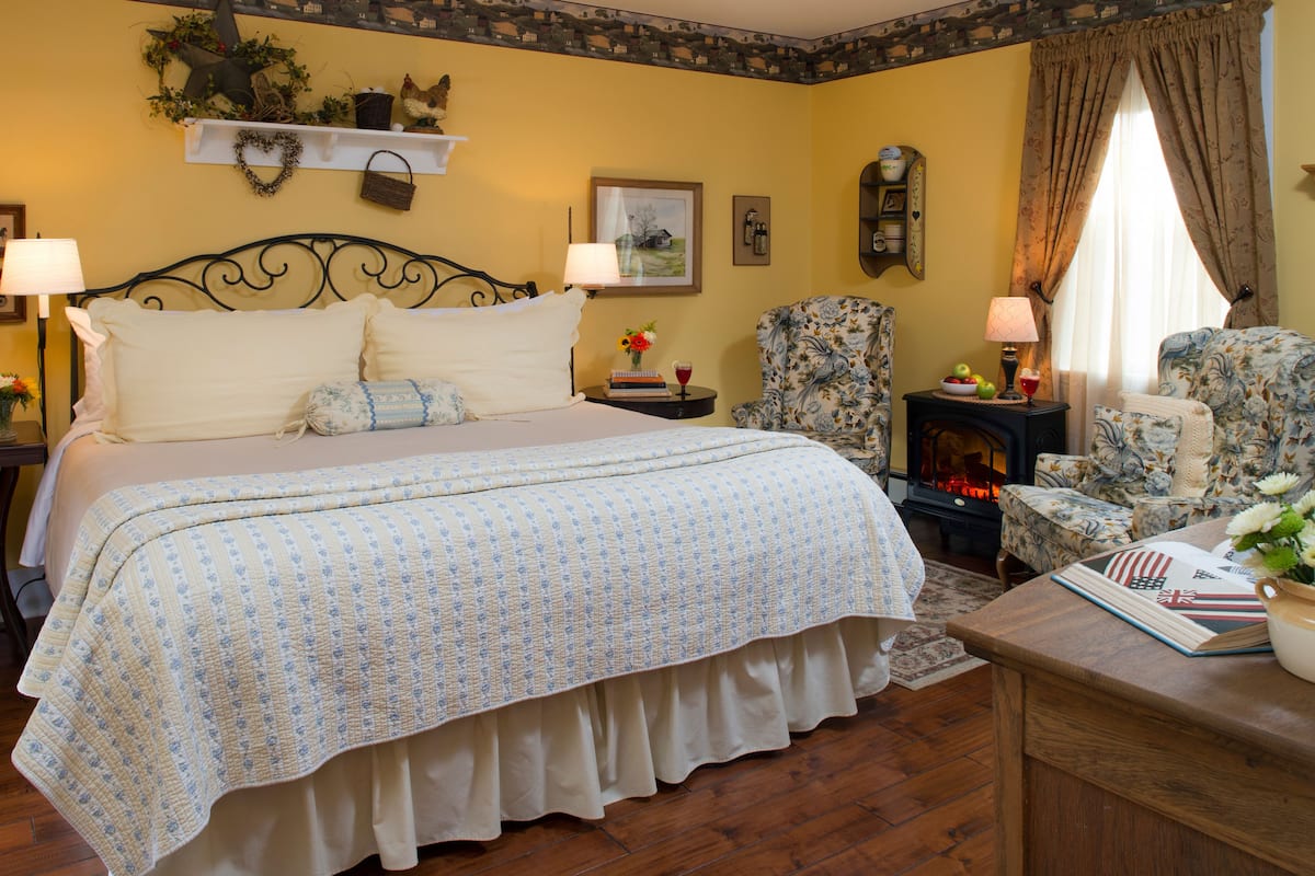 A bedroom with a large bed, a chair, a small table, and a fireplace.