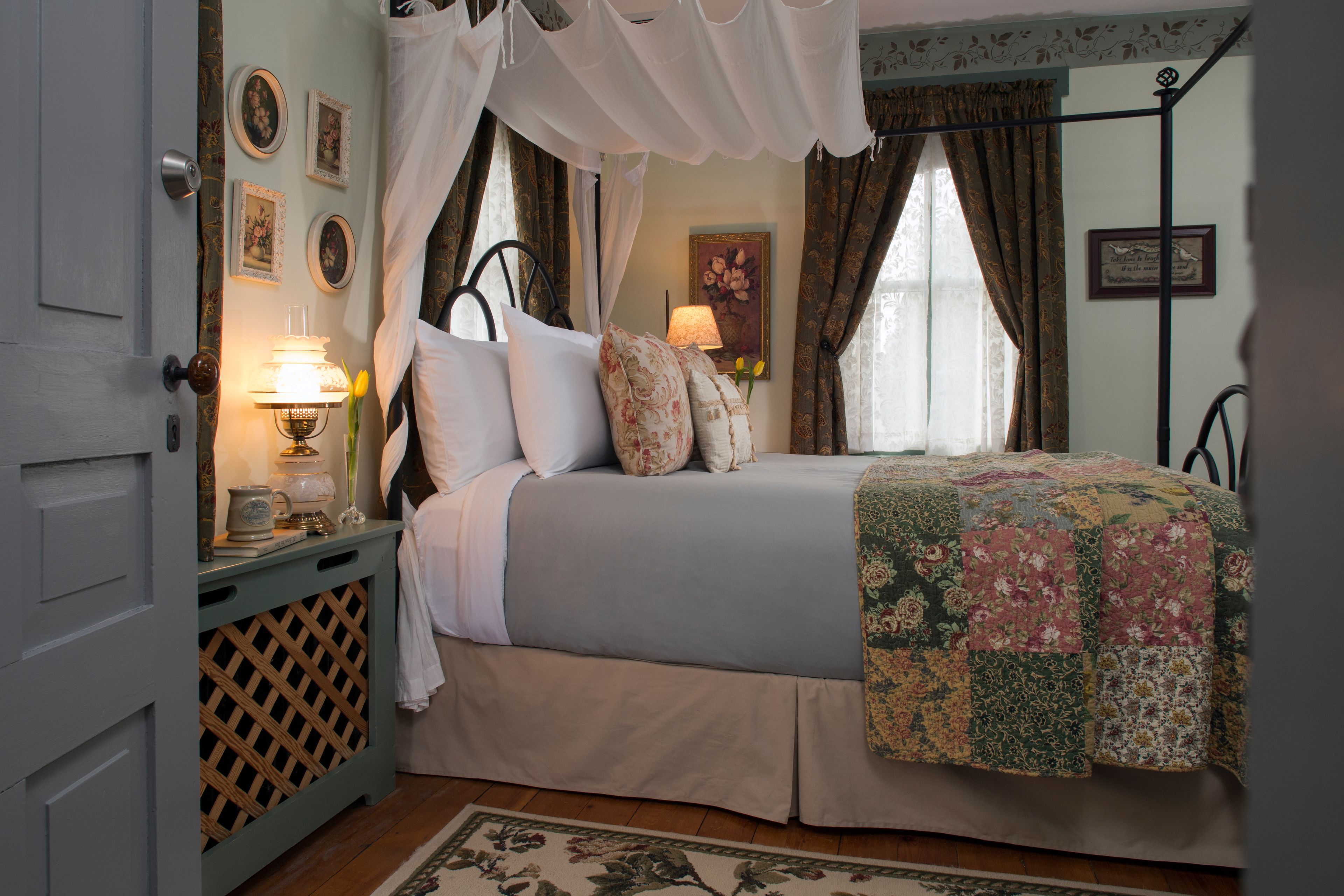 Quarto com cama de dossel, mesa de cabeceira com abajur e decoração floral.
