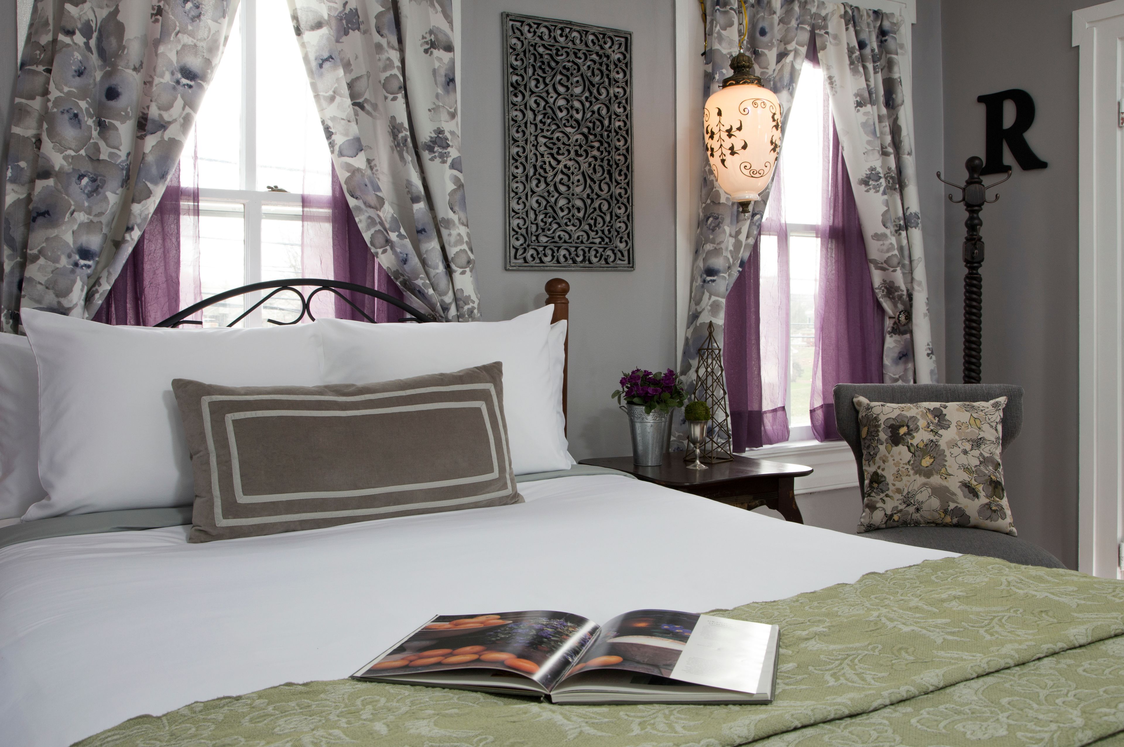 A neatly made bed with a book, a decorative wall piece, and a lamp.