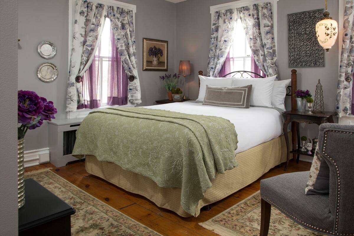 A bedroom with a bed, a nightstand, a chair, and a window with curtains.