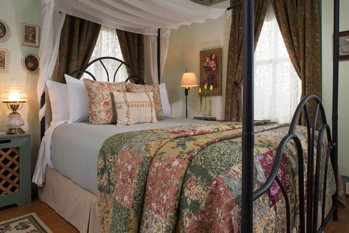 A four-poster bed with a canopy, floral bedding, and a bedside table with a lamp.