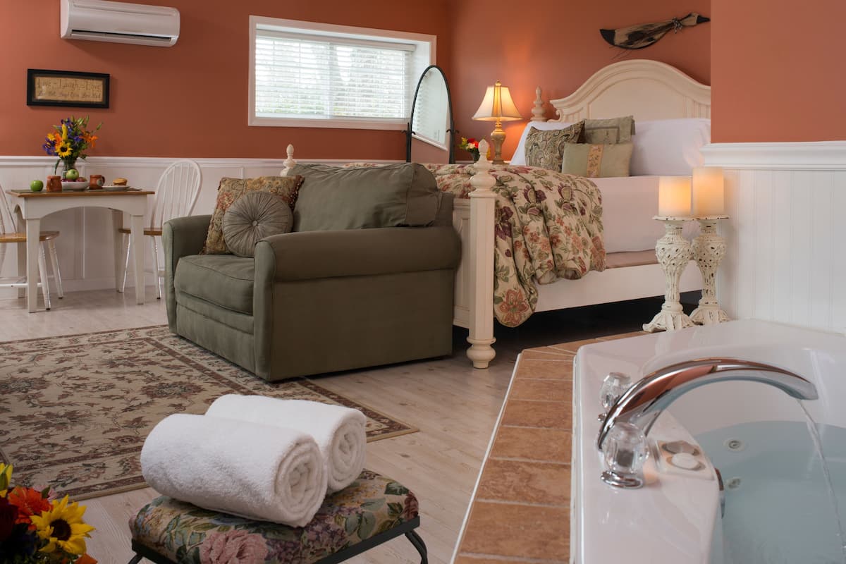 A bedroom with a bed, bedside table, lamp, and a bathroom with a sink and tub.