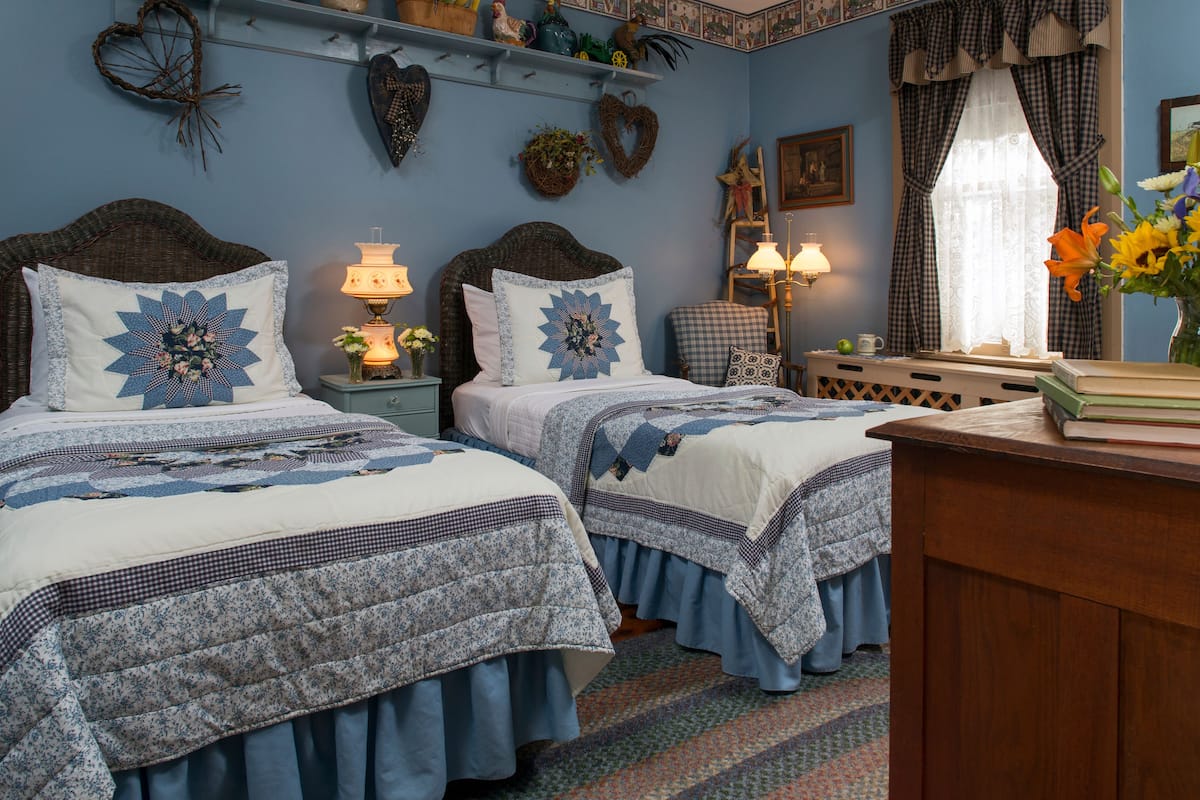 A bedroom with two beds, a nightstand with a lamp, a dresser, and a window with curtains.
