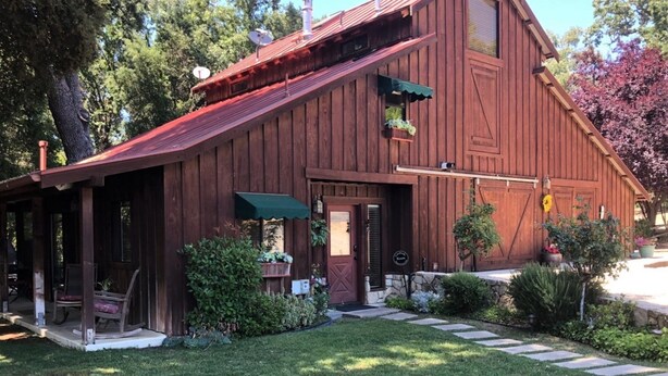 A rustic wooden barn with a red roof, a covered porch, and a stone foundation. - Creekside Inn of Paso Robles (Paso Robles)