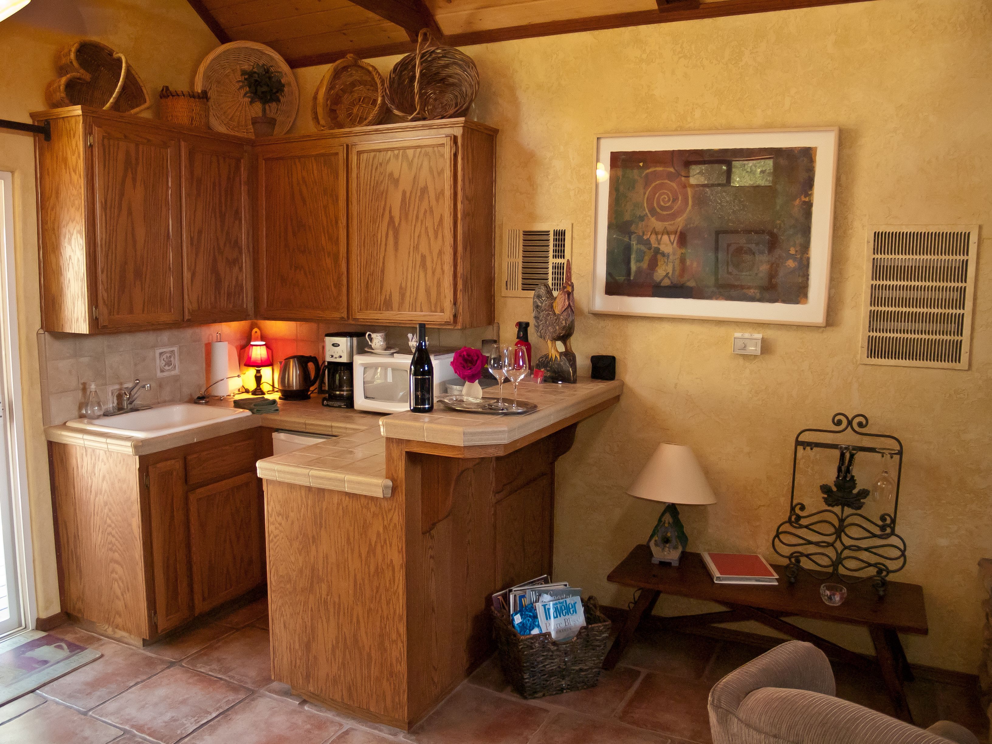 Una cocina con armarios de madera, un microondas, un lavamanos y una pequeña zona de comedor con una mesa y una silla.