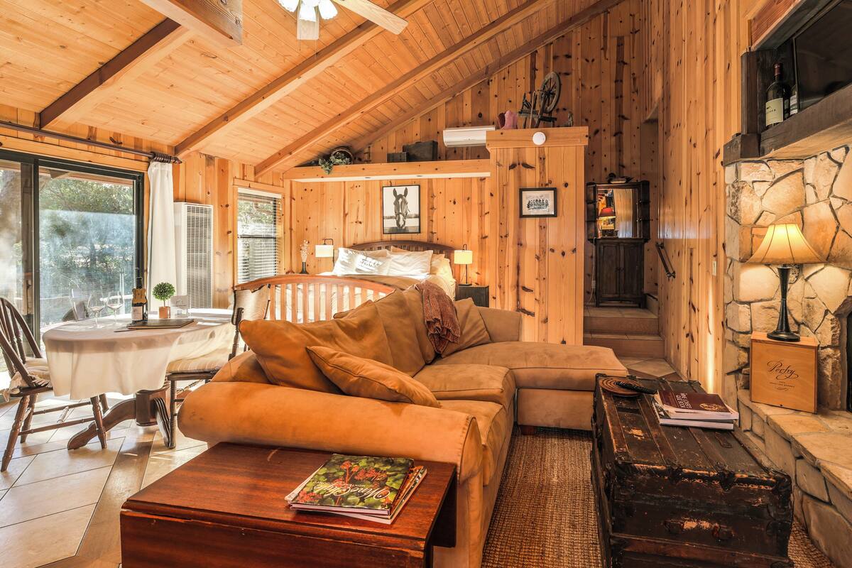 A cozy wooden cabin interior with a sofa, a table with a book, a fireplace, and a dining area with a table and chairs.
