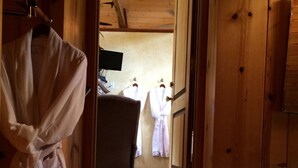 A wooden interior with a robe hanging on the left, a wooden door, and a glimpse of a room with a bed and a mirror. - Creekside Inn of Paso Robles (Paso Robles)