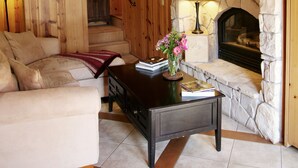 A cozy living room with a stone fireplace, wooden walls, a sofa, and a coffee table with books and flowers. - Creekside Inn of Paso Robles (Paso Robles)
