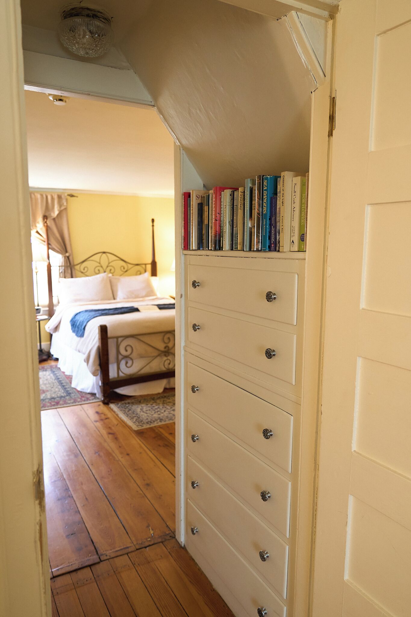 Una camera da letto con un letto, una cassettiera piena di libri e un pavimento in legno.