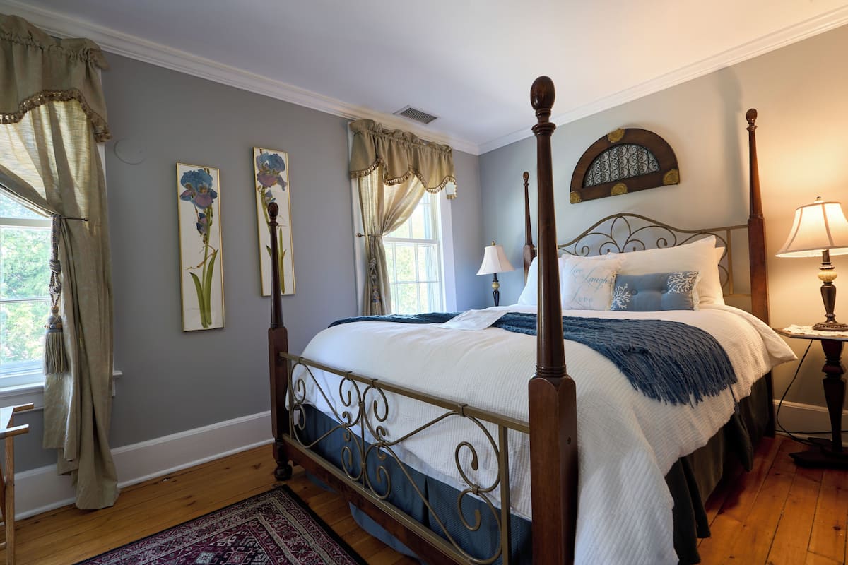 A four-poster bed with a headboard, a bedside table with a lamp, and a window with curtains.