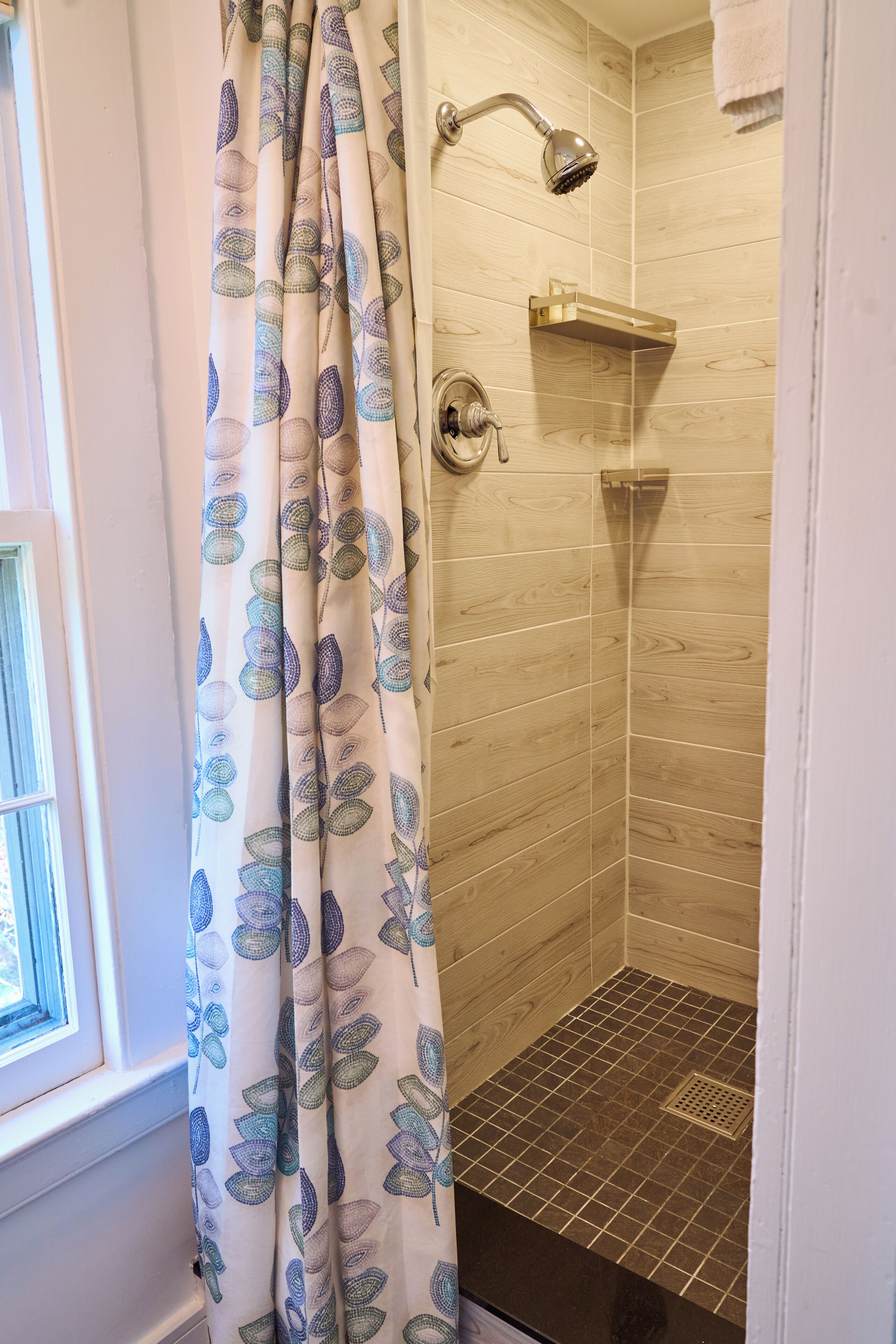 A shower with a wooden wall, a showerhead, and a curtain with leaf patterns.