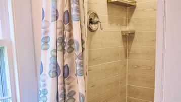 A shower with a wooden wall, a showerhead, and a curtain with leaf patterns.