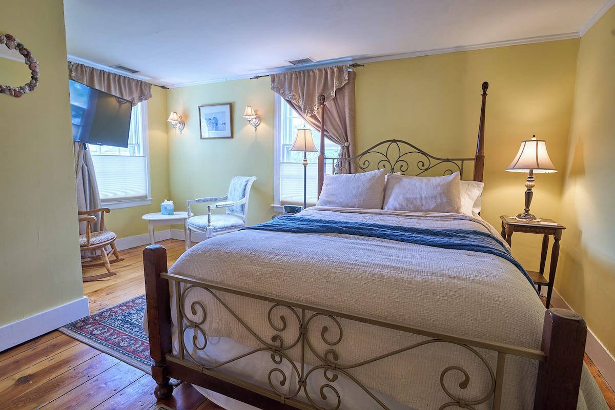 A bedroom with a four-poster bed, a rocking chair, a small table, and a lamp.