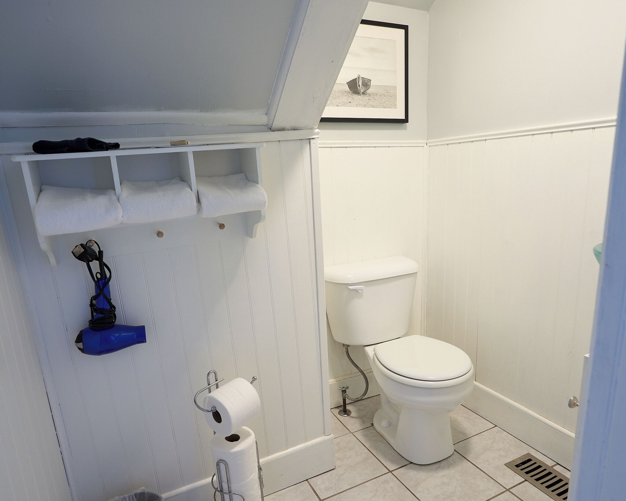 Un baño con inodoro, rollo de papel higiénico, toallero y un cuadro enmarcado en la pared.