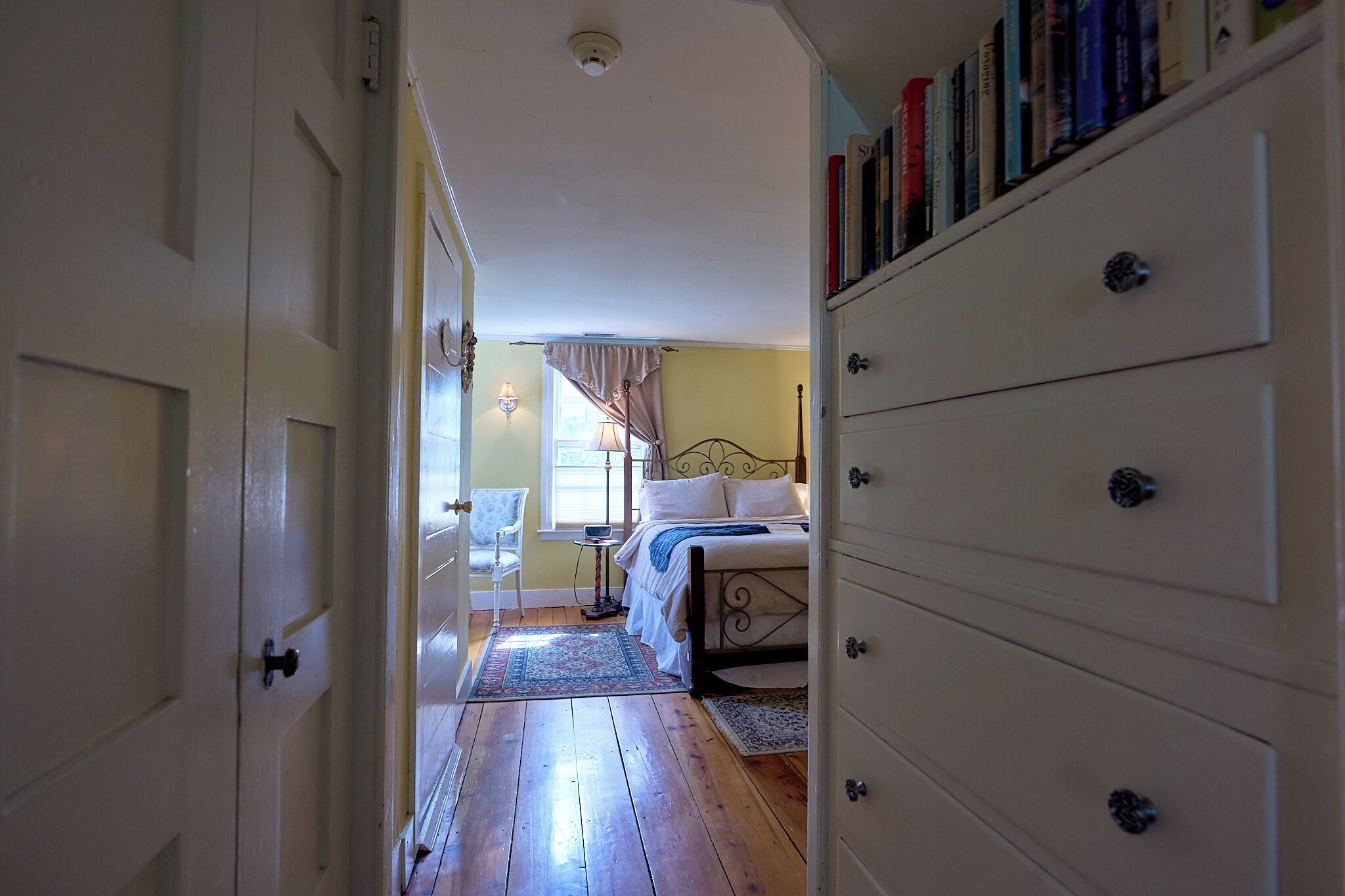Un dormitorio con cama, cómoda, silla y ventana con cortinas.