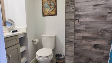 Une salle de bain comprenant des toilettes, un lavabo avec un miroir, un rouleau de papier toilette et une poubelle.