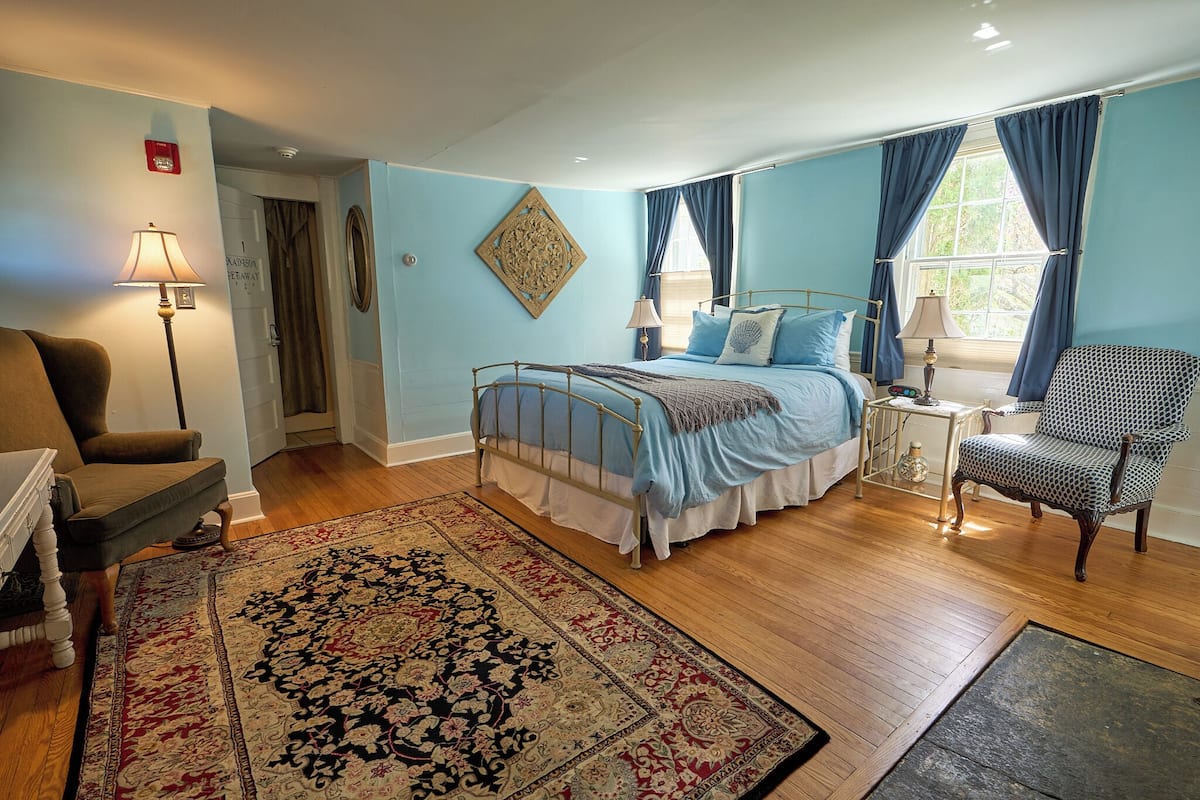A bedroom with a bed, a chair, a lamp, a rug, and a window with curtains.