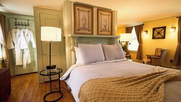 A hotel room with a bed, bedside lamps, a small table, a chair, and a wardrobe with robes.